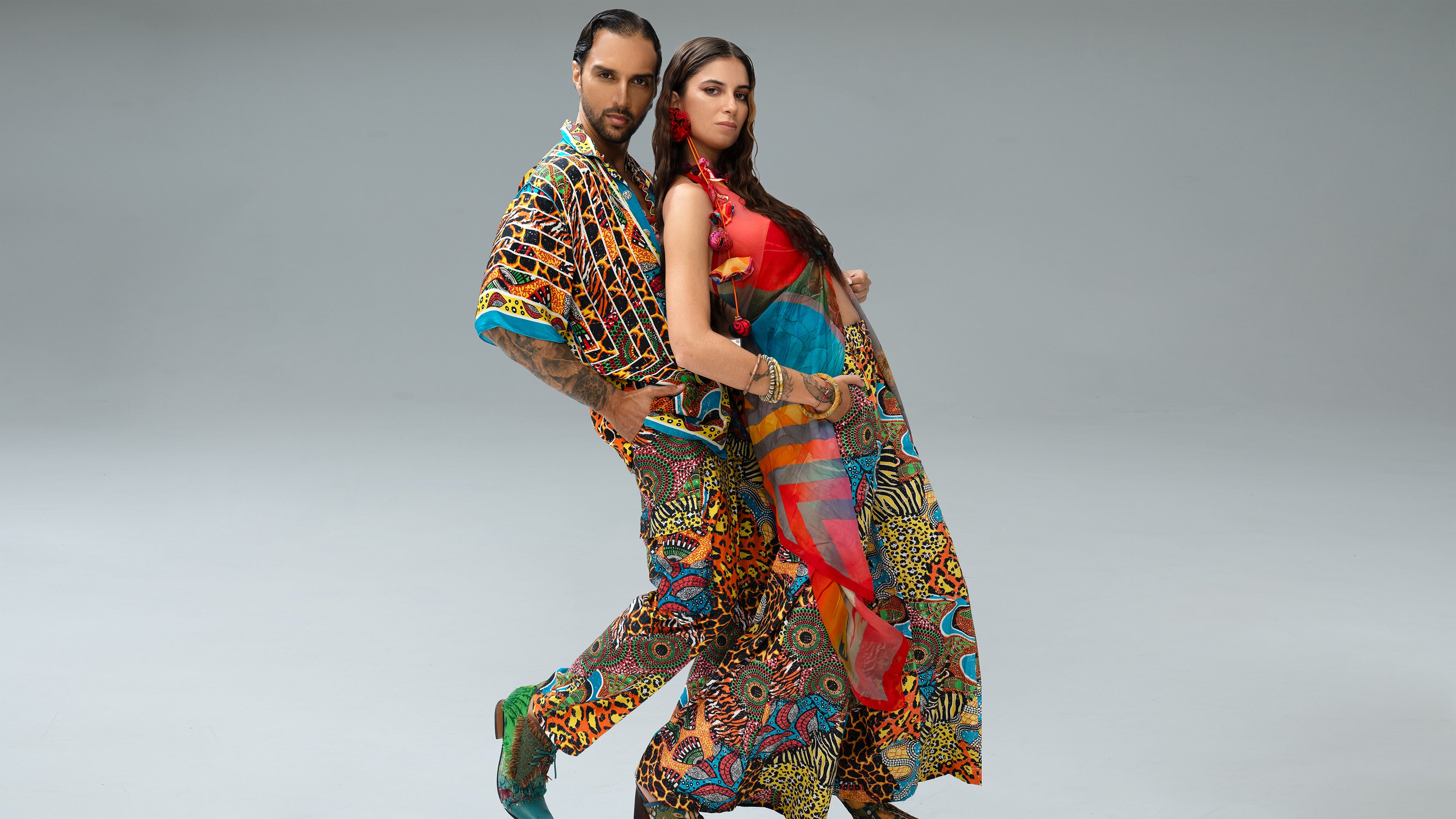 High-fashion editorial photograph of a male and female model in a dynamic, intertwined pose, both wearing vibrant, multi-color patterned ensembles from the Paul Ropp bohemian luxury collection against a minimal studio background.

available in-store in Bali, Indonesia